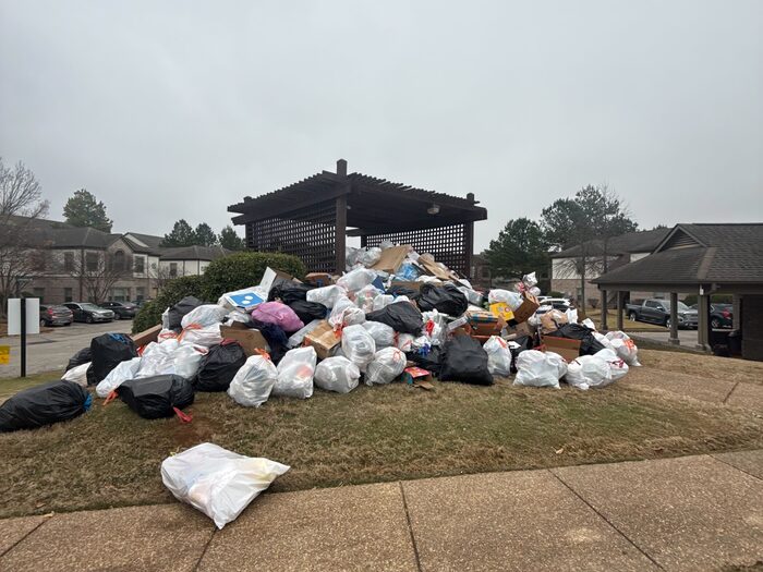 Bagged waste piled across a lawn beside an apartment bin store