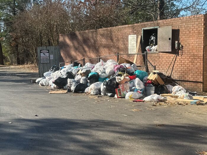 A line of bagged waste along a brick wall in a parking lot