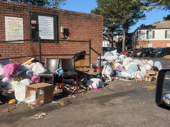 Bags, boxes and furniture piled against the wall of a bin enclosure