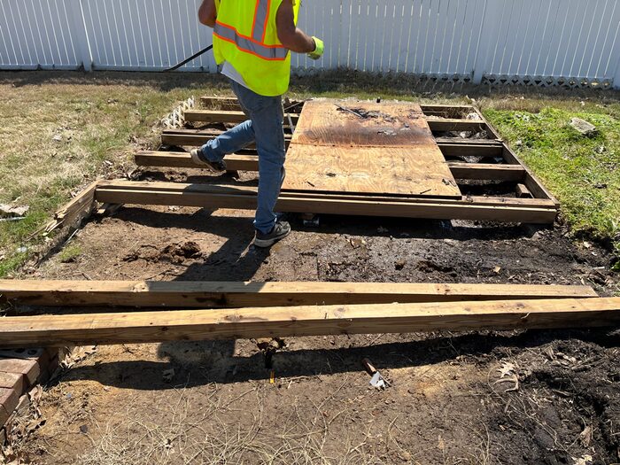 A crew member lifting the floor joists of a shed once its walls are down
