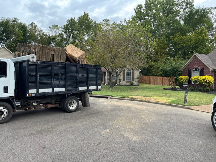 A truck loaded with old fencing and rolled carpet parked on a residential street
