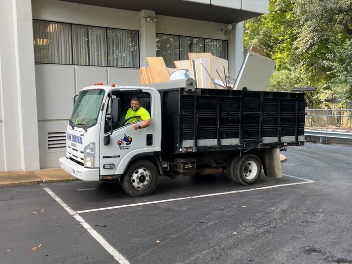 A crew member in the cab of a loaded truck outside an office building
