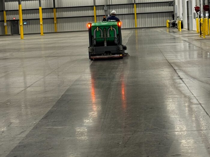 A ride-on sweeper working the floor of an empty warehouse